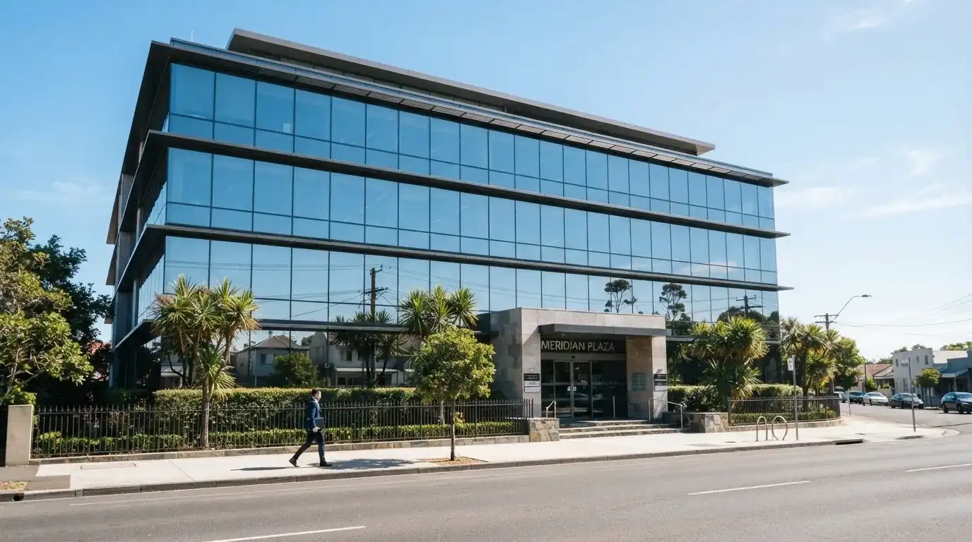 Un edificio de oficinas moderno con cristales reflectantes bajo un cielo despejado, visto desde una calle tranquila.